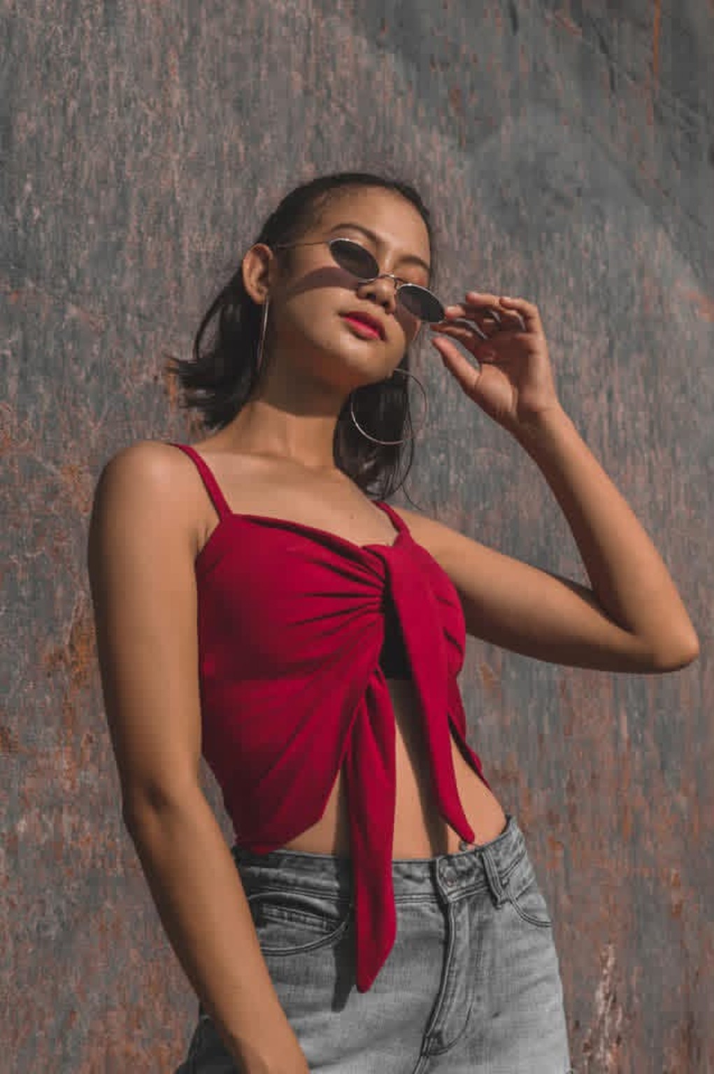 Woman in a red top and sunglasses beside a textured wall